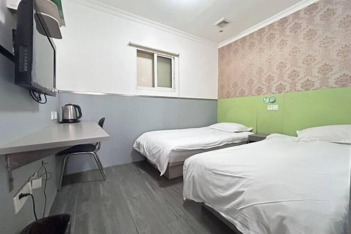 Habitación de hotel con dos camas, un escritorio con hervidor, una silla, un ventanal y una pared con diseño decorativo.