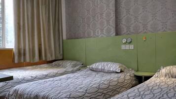 A room with two beds, a window with curtains, and a green headboard.