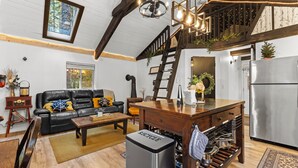 En rummelig stue med en sort lædersofa, et træsofabord og et indbygget vinskab. En trappe fører op til et plan med en balkon.