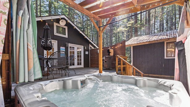 Et område med jacuzzi, en træterrasse, et overdækket siddeområde og udsigt til et skovområde.
