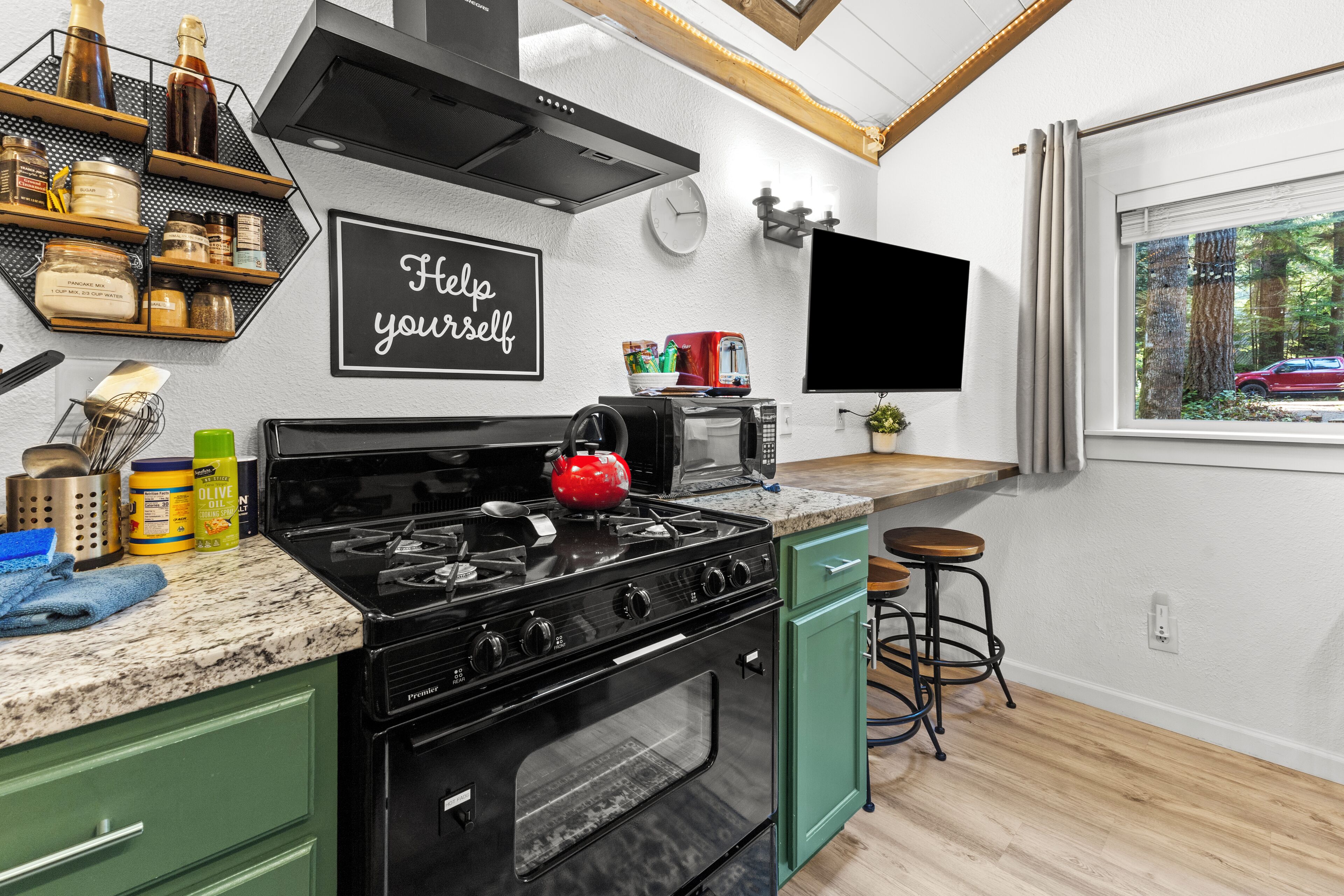 A modern kitchen with a gas stove, a microwave, and a toaster. There is a sign that says 'Help yourself' on the wall.