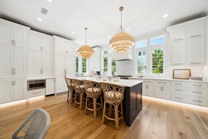 A modern kitchen with white cabinets, a central island with bar stools, pendant lighting, and large windows.
