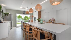 Una cucina moderna con una grande isola, sedie in legno, lampade a sospensione e vista sull'esterno.