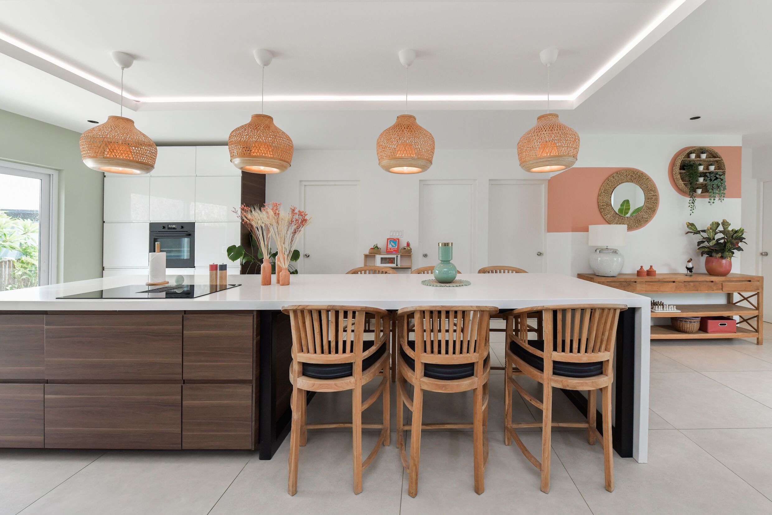 Una cocina moderna con una isla grande, sillas de madera, luces colgantes y una mesa de comedor.