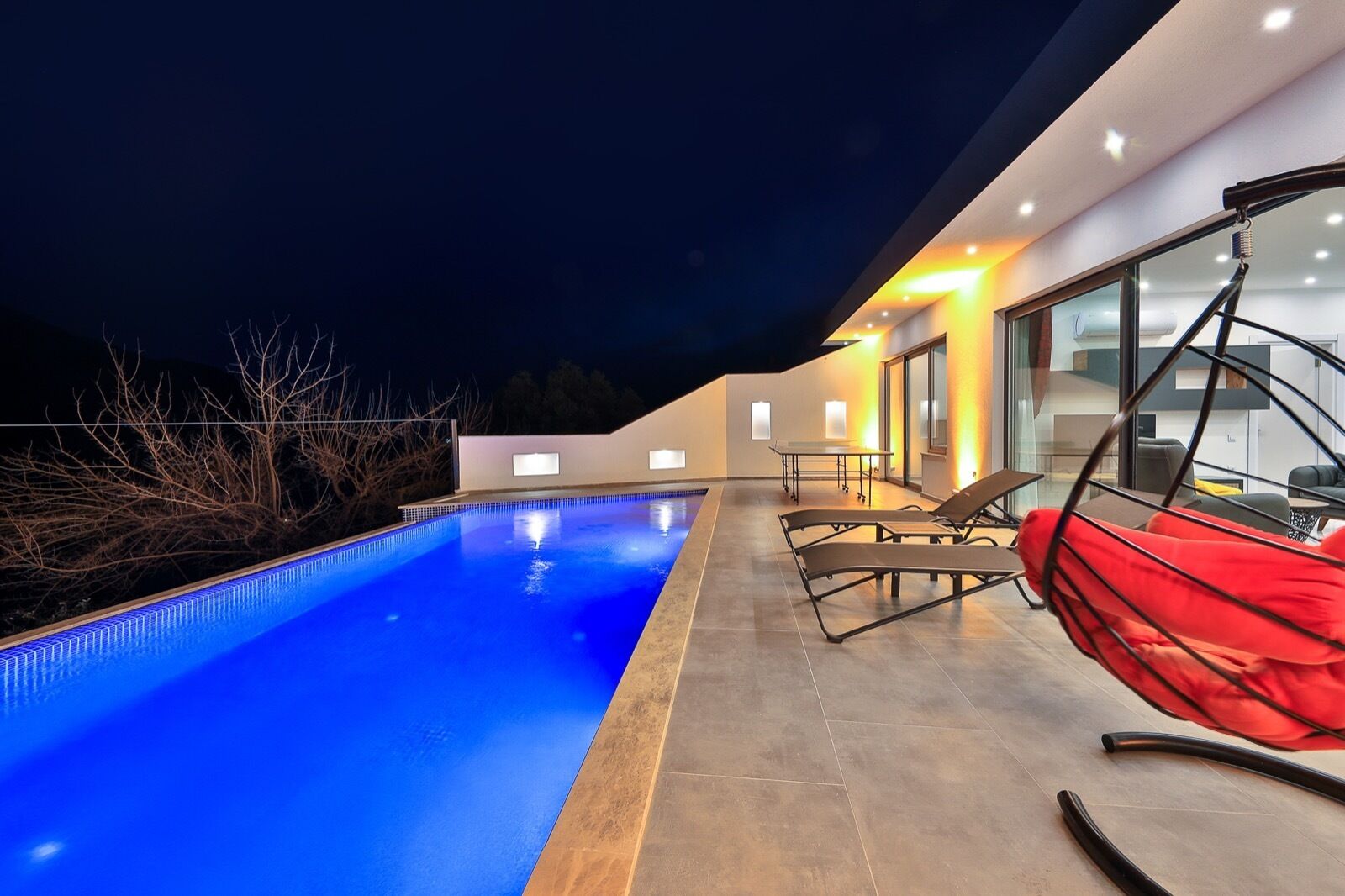 Un área de piscina moderna al aire libre con piscina azul cristalina, sillas de descanso y una hamaca roja.