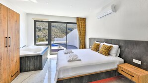 Un dormitori modern amb un llit gran, una banyera integrada i vista a un paisatge de muntanya.