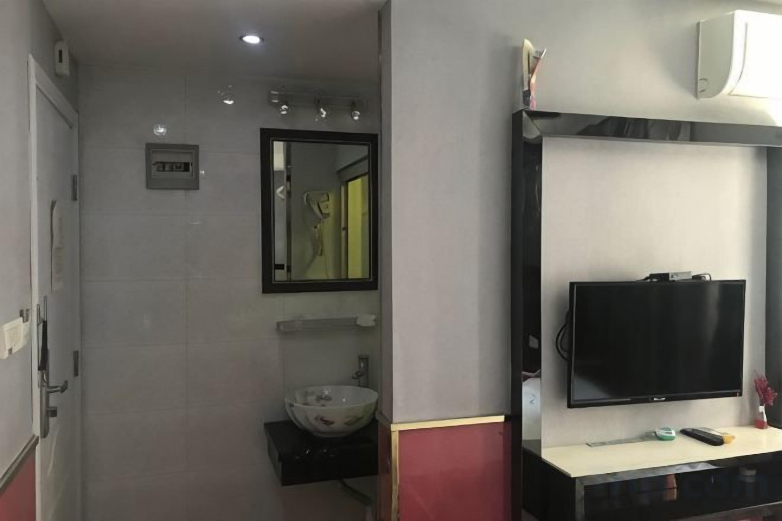 A bathroom with a sink, mirror, and a mounted television.