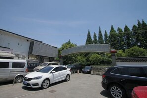 Um estacionamento com vários carros, um edifício com telhado curvo e árvores ao fundo.