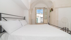 Une chambre avec un grand lit, du linge de lit blanc, un balcon avec vue et une porte blanche.