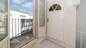 Un couloir étroit avec une porte blanche et une porte vitrée donnant sur un balcon.
