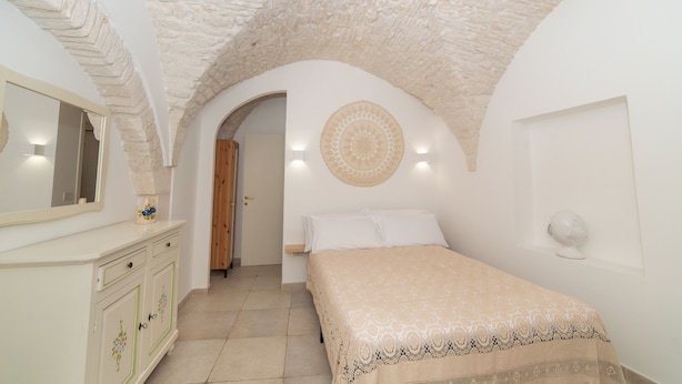Une chambre avec un plafond en pierre, un lit recouvert d’une couvre-lit à motifs, une commode avec des tiroirs, un miroir et un élément décoratif circulaire fixé au mur.