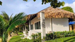 A small, single-story building with a thatched roof, surrounded by well-maintained greenery and palm trees. - Villa Sereno Beachfront Koh Samui (Koh Samui)
