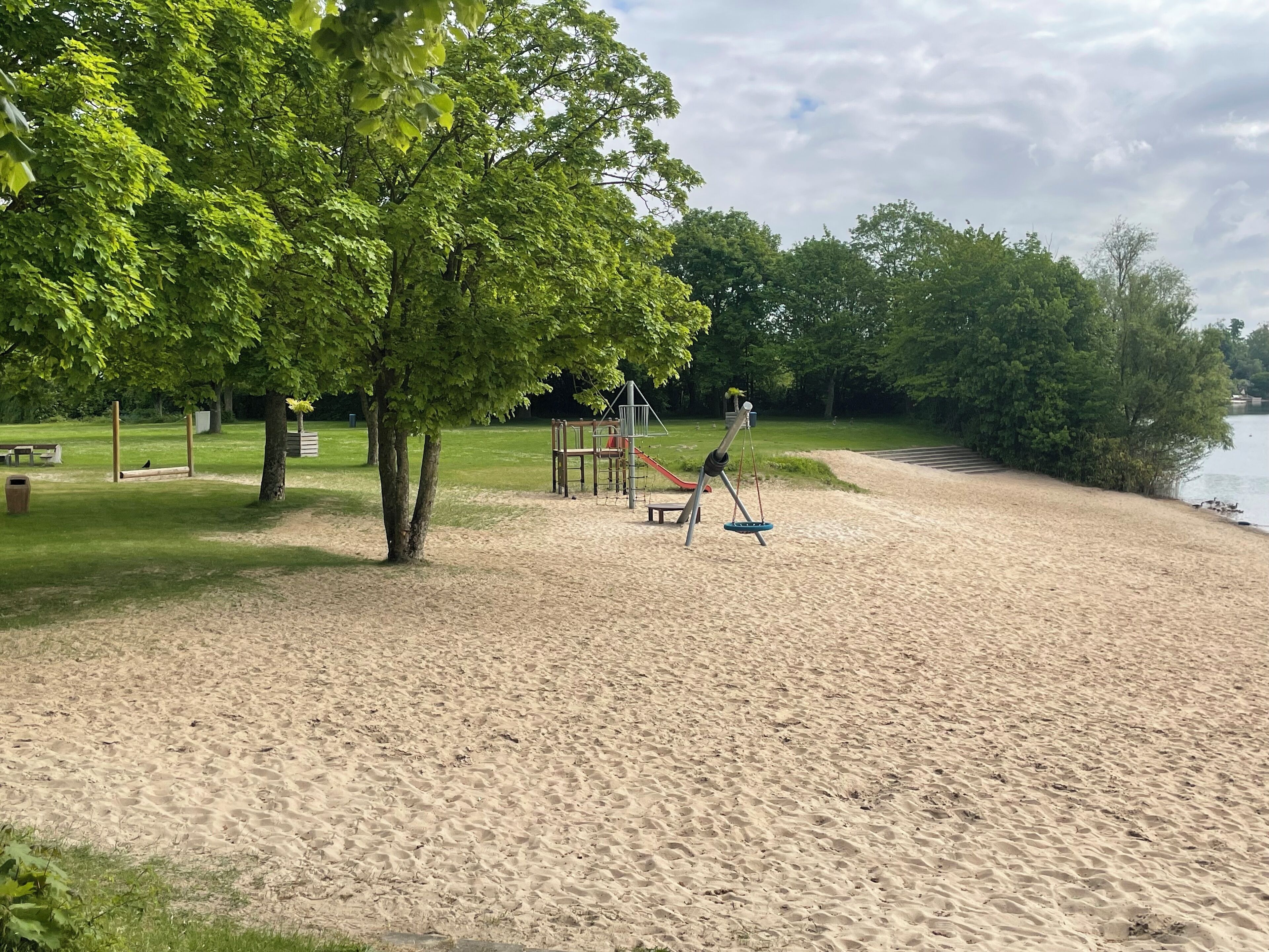 A sandy beach with a playground and a picnic area.
