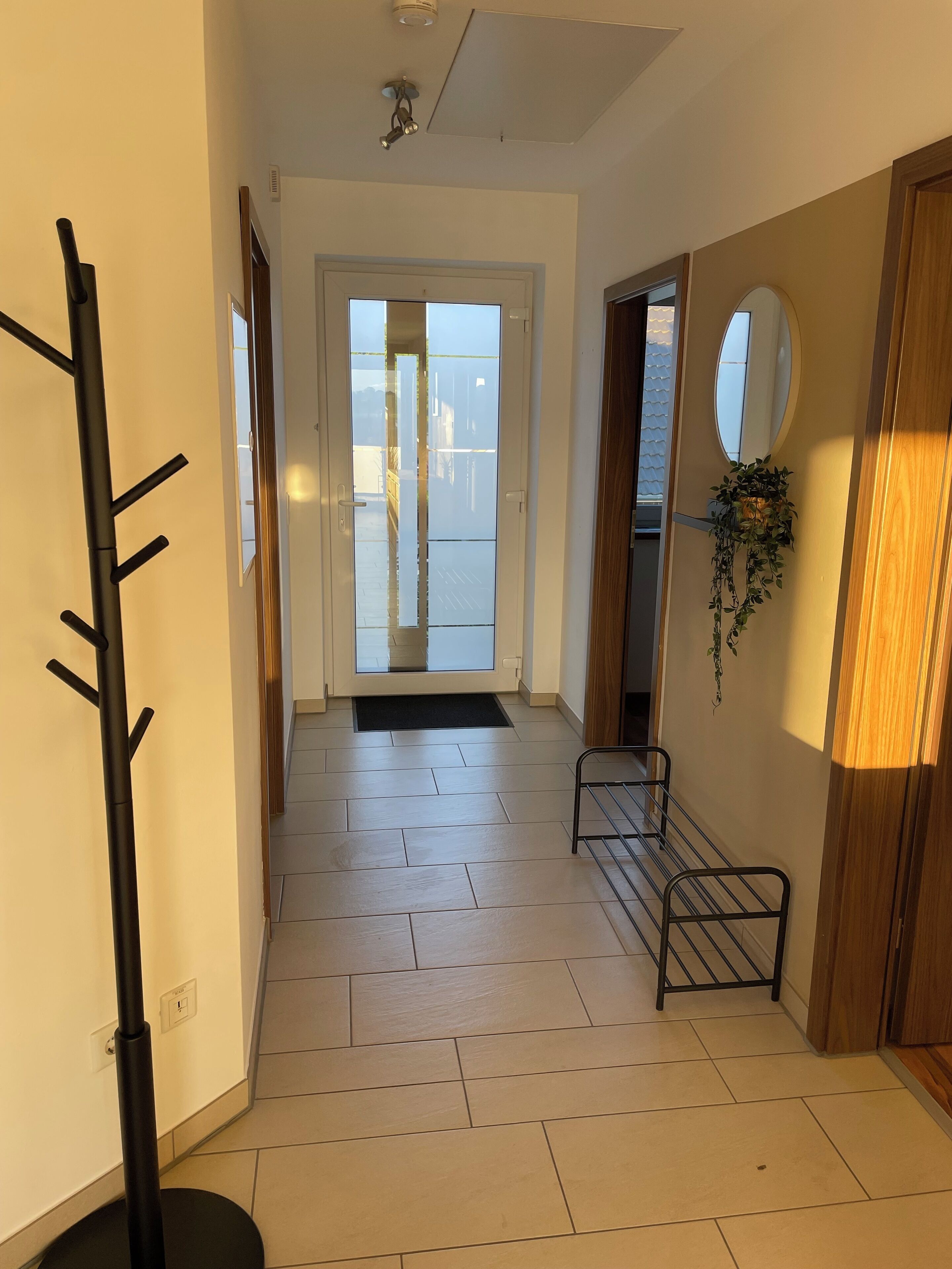A hallway with a coat rack, a small bench, a door leading outside, and a wall-mounted mirror.