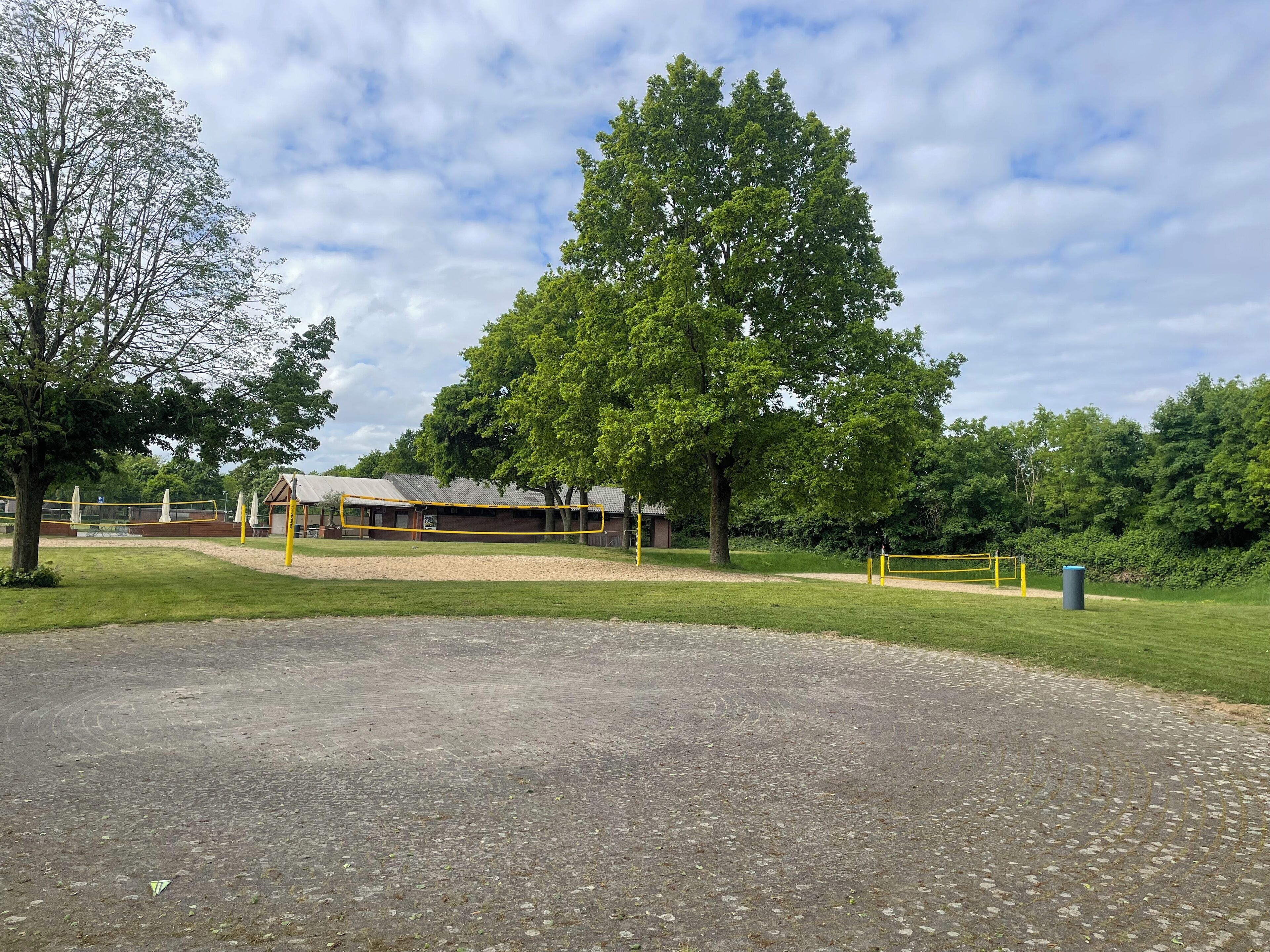 A playground with a yellow fence, a covered seating area, and a large tree in the background.