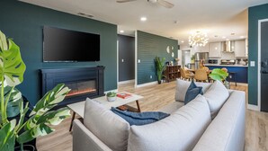 A modern living room with a fireplace, a sofa, a coffee table, and a television. - Pool, Hot Tub Heating, BBQ, AC & Private Yard, Pet Friendly, 10mins to JTNP! (Joshua Tree)