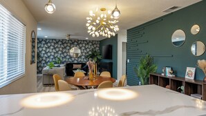 A modern dining area with a marble table, pendant lighting, and a green accent wall. - Pool, Hot Tub Heating, BBQ, AC & Private Yard, Pet Friendly, 10mins to JTNP! (Joshua Tree)