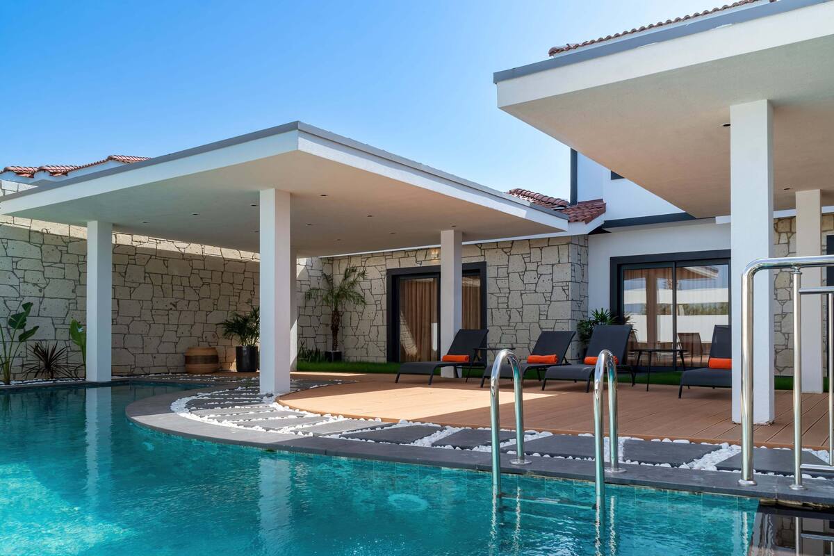 A pool area with a stone wall, lounge chairs, and a covered patio.