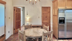 Une table à manger en bois avec des chaises, un lustre, des meubles en bois et un réfrigérateur en acier inoxydable.