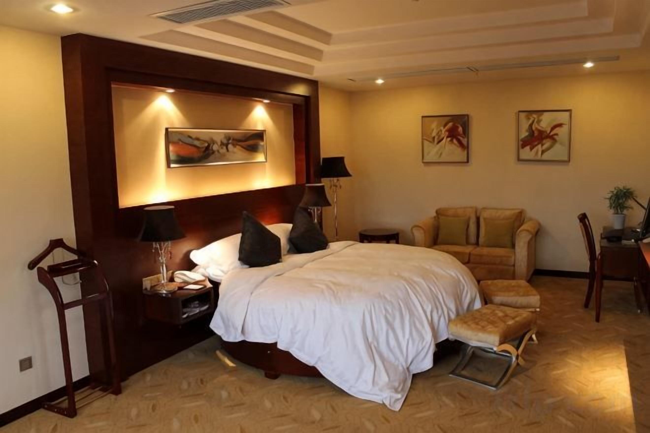 A hotel room with a large bed, a bedside table, a chair, and artwork on the walls.