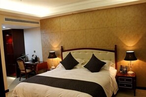 A hotel room with a large bed, two bedside lamps, a nightstand, and a desk with a chair. - Teenly Garden International Hotel (Pingxiang)