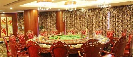 Un comedor formal con una mesa redonda, sillas tapizadas en rojo y adornos ornamentales en las paredes.