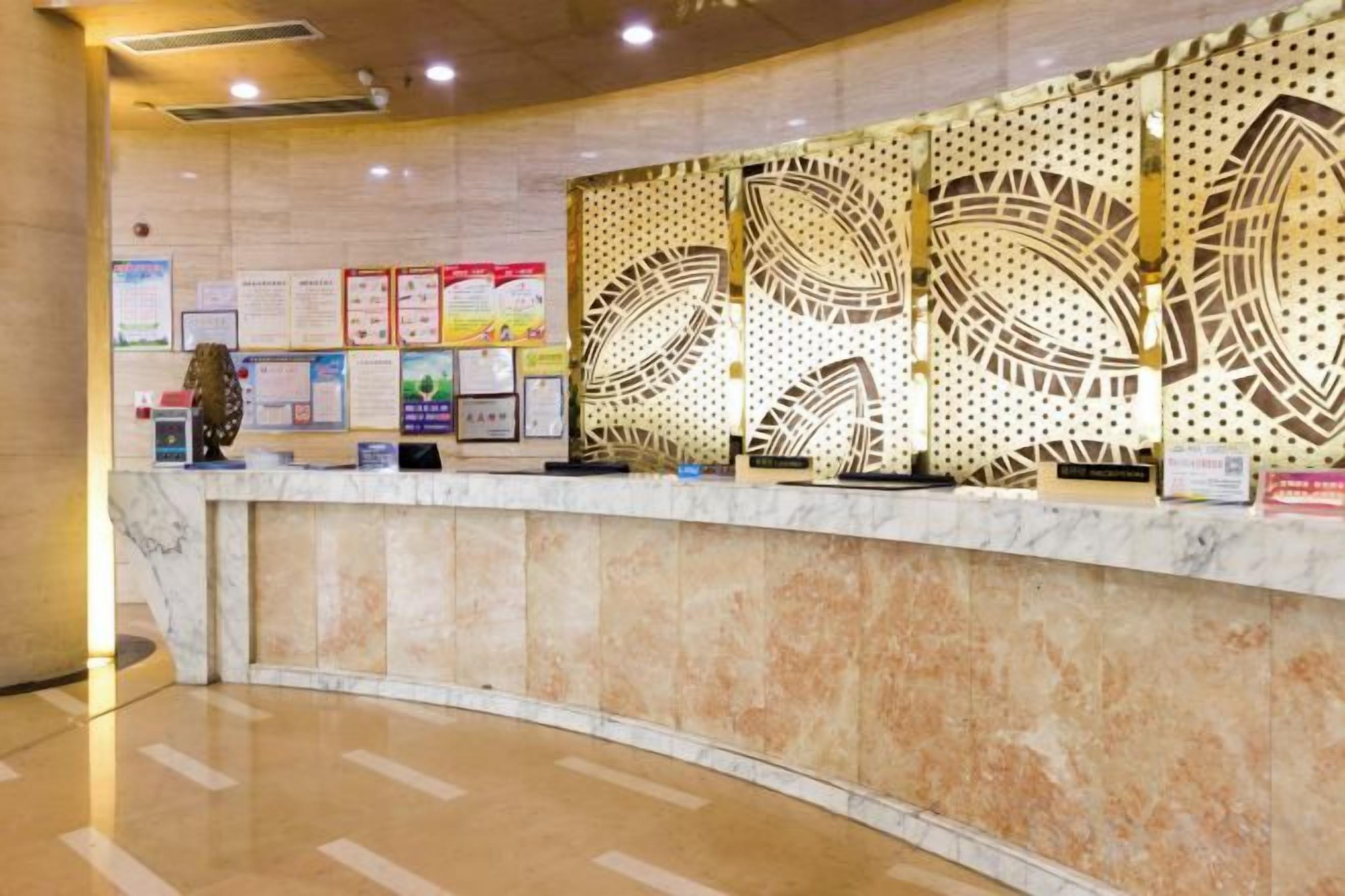 Un comptoir d’accueil avec un revêtement en marbre, des affiches d’information et un mur décoratif orné de motifs géométriques.