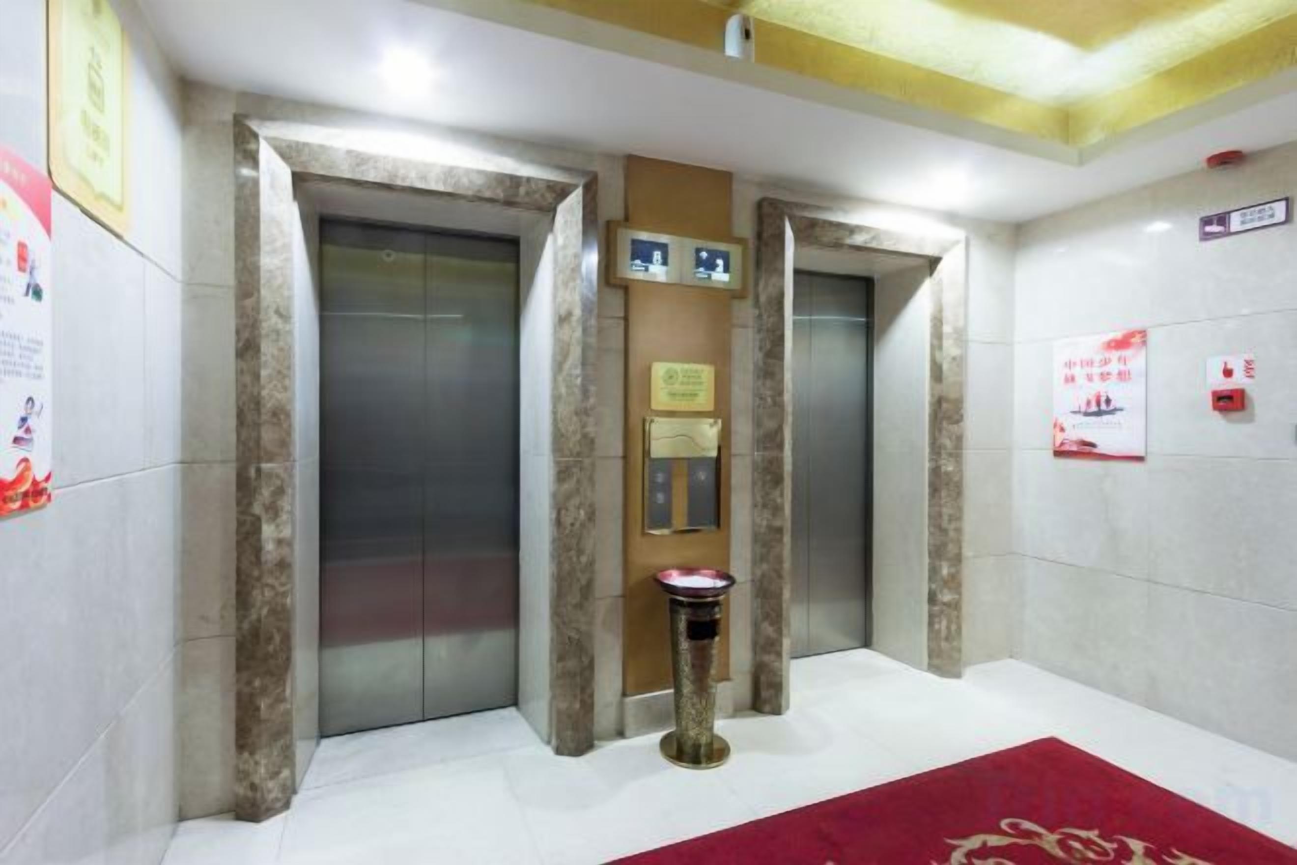 Zona de ascensores con dos elevadores, un cesto de basura y una alfombra roja.