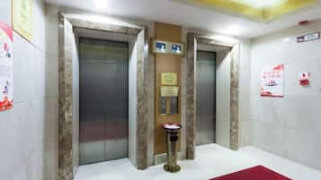 Zona de ascensores con dos elevadores, un cesto de basura y una alfombra roja.