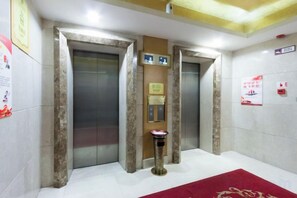 Zona de ascensores con dos elevadores, un cesto de basura y una alfombra roja.