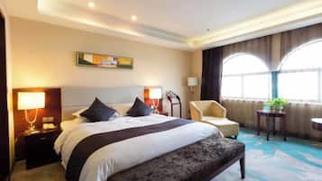 A hotel room with a large bed, bedside tables, a chair, a round table, and a window with curtains.
