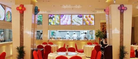 A restaurant with round tables, red chairs, and a kitchen area visible through the glass wall.