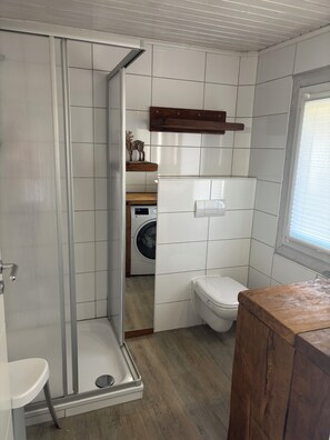 Un baño pequeño con ducha, inodoro y lavadora.