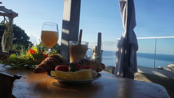Una mesa con un plato de fruta, un vaso de jugo y una taza de café, con vista a un paisaje marítimo.