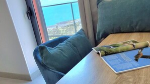 Una habitación con una mesa de madera, un cojín verde y vista al mar a través de una ventana.