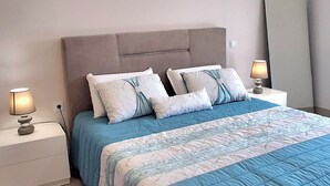 Un dormitorio con cama, mesitas de noche, lámpara y espejo.