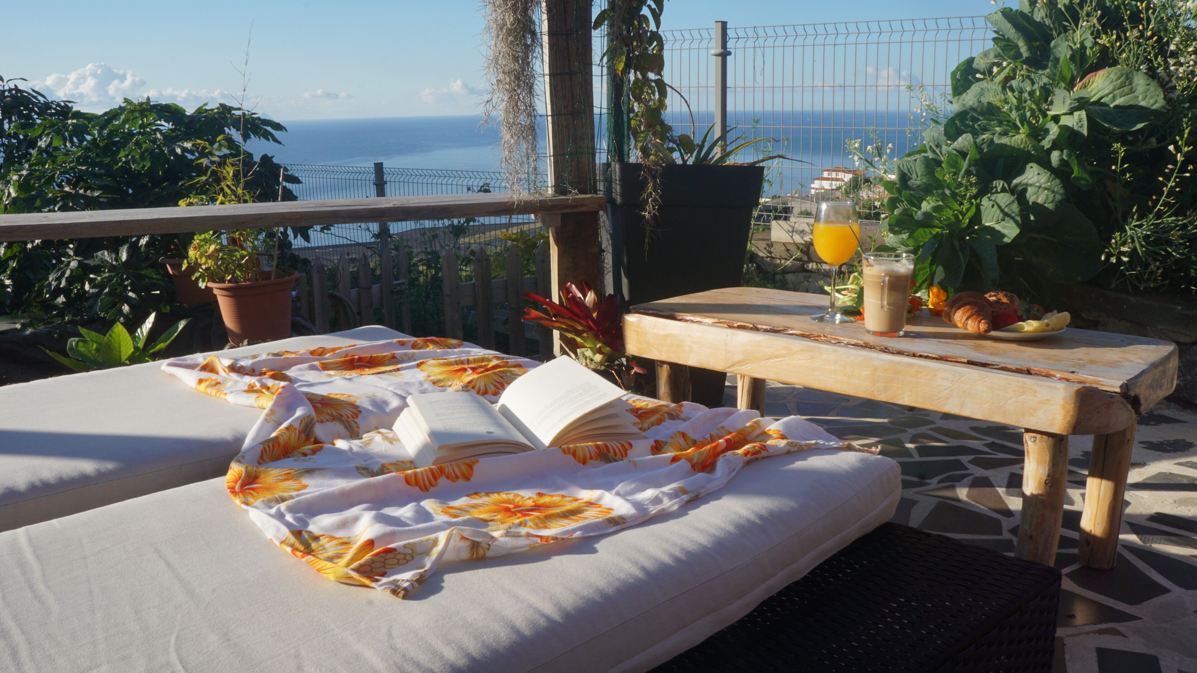 A balcony with two beds, a table with breakfast items, and a view of the sea.