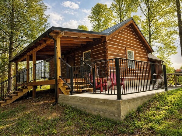 A log cabin with a porch, a staircase, and a concrete platform.