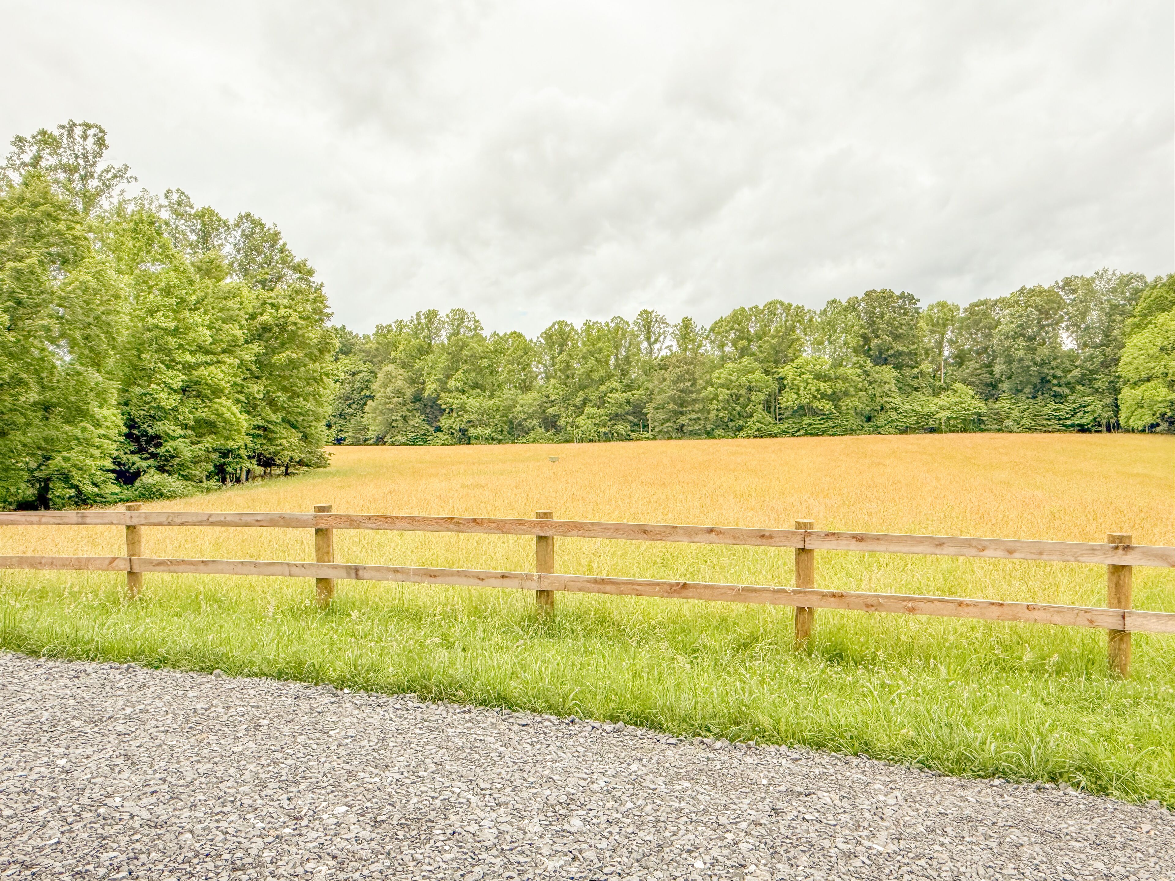 Un paysage rural avec un chemin de gravier, une clôture en bois et un champ cultivé.