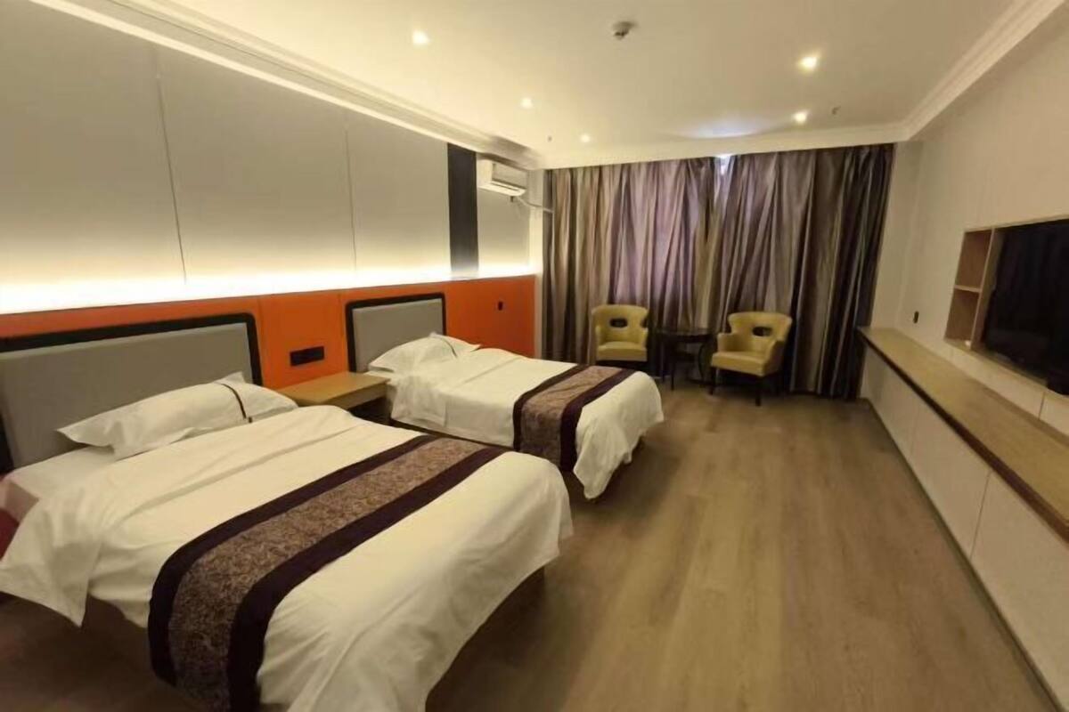 A hotel room with two beds, a desk, two chairs, a TV, and a curtain.