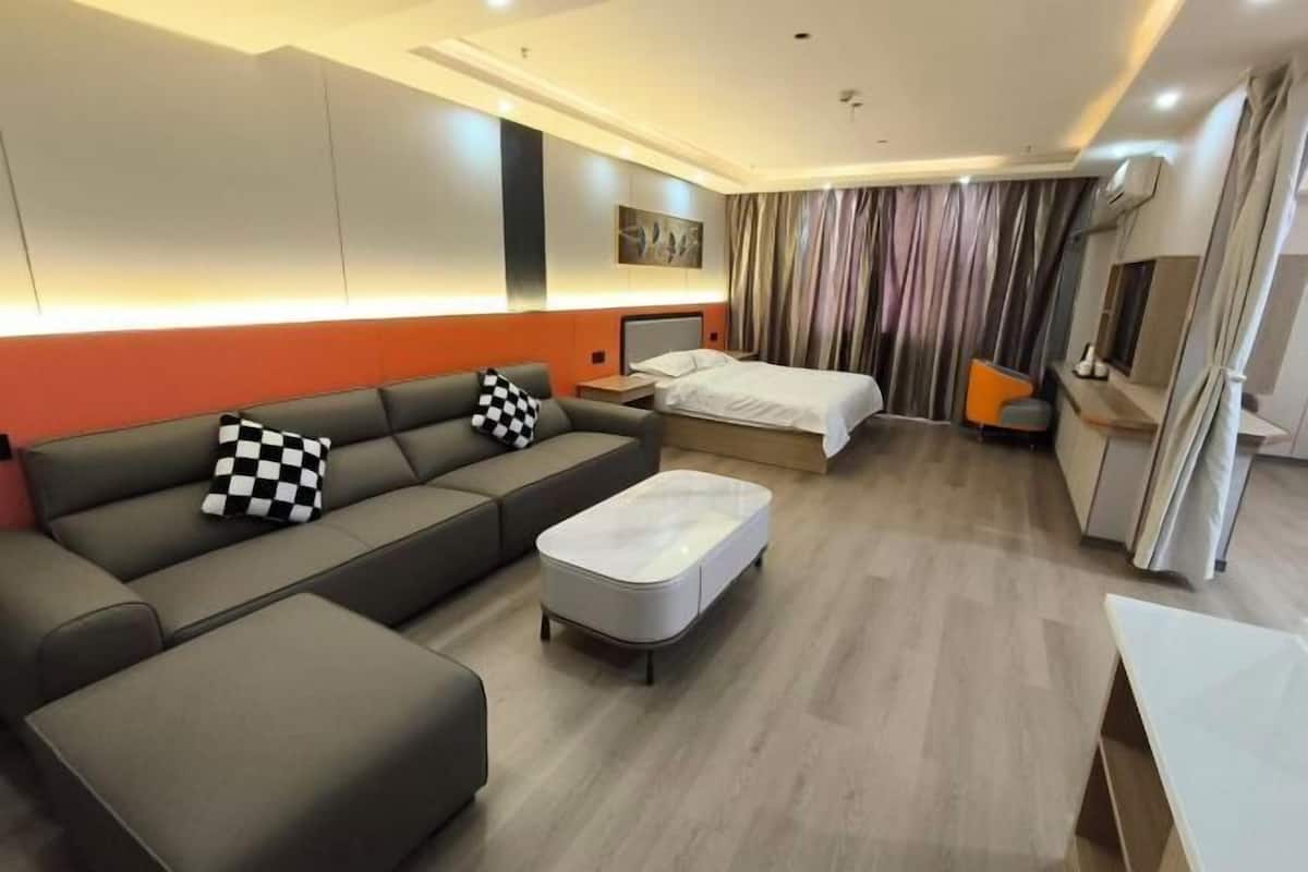 A modern hotel room with a sofa, ottoman, bed, and a small table.
