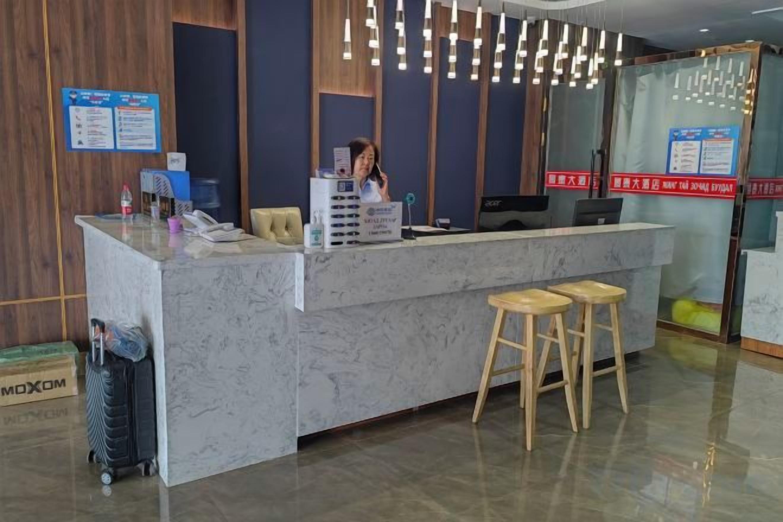 A reception desk with a marble top, wooden stools, and a hanging light fixture.