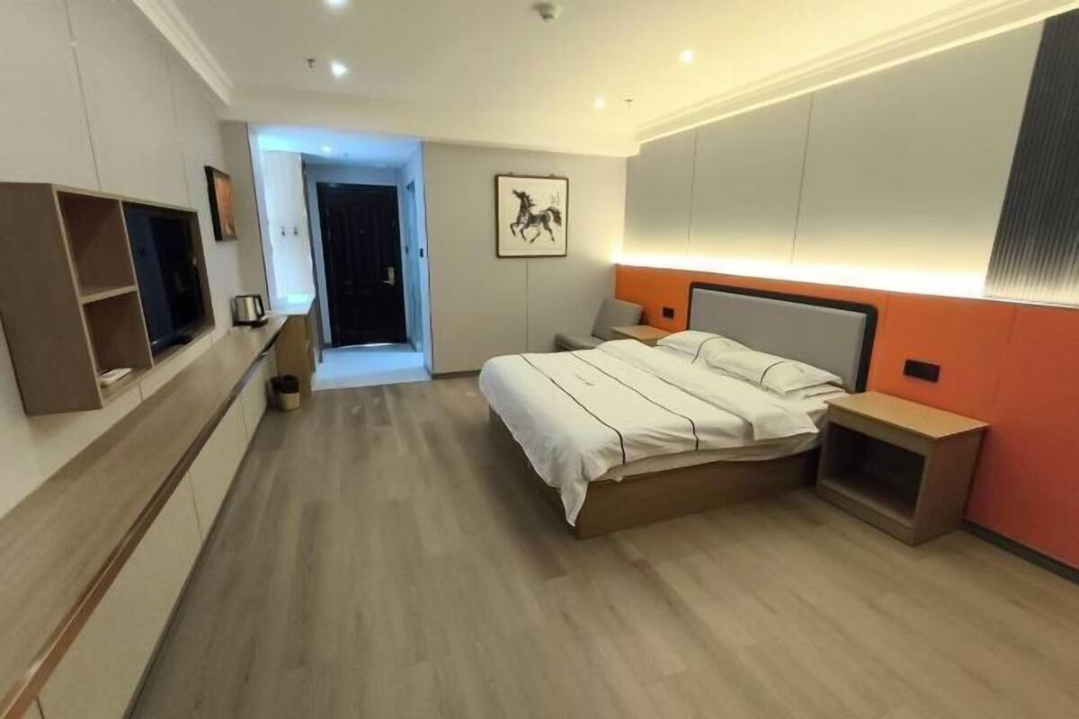 A modern hotel room with a bed, bedside tables, a TV, and a door leading to a balcony.