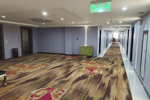 Pasillo de hotel con alfombra estampada, puertas a la derecha y un cubo de basura verde.