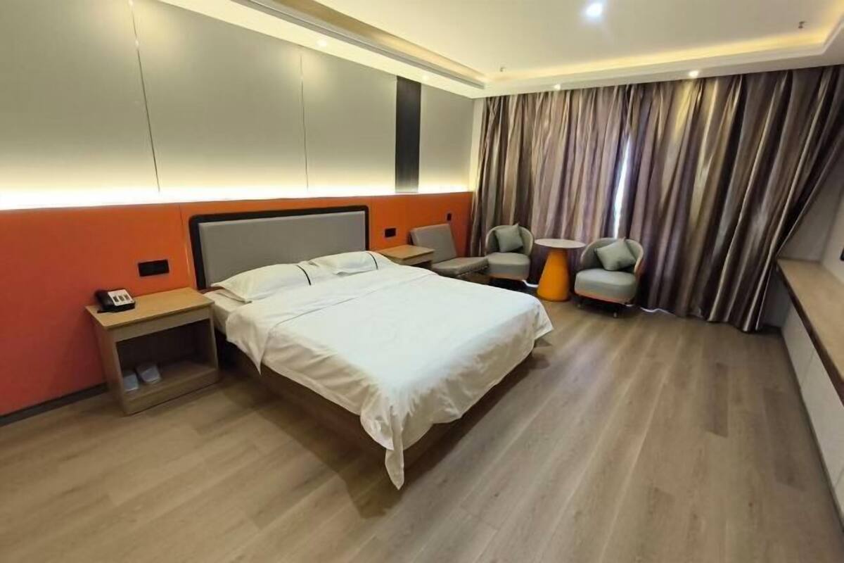 A hotel room with a bed, bedside tables, a chair, a small table, and a curtain.