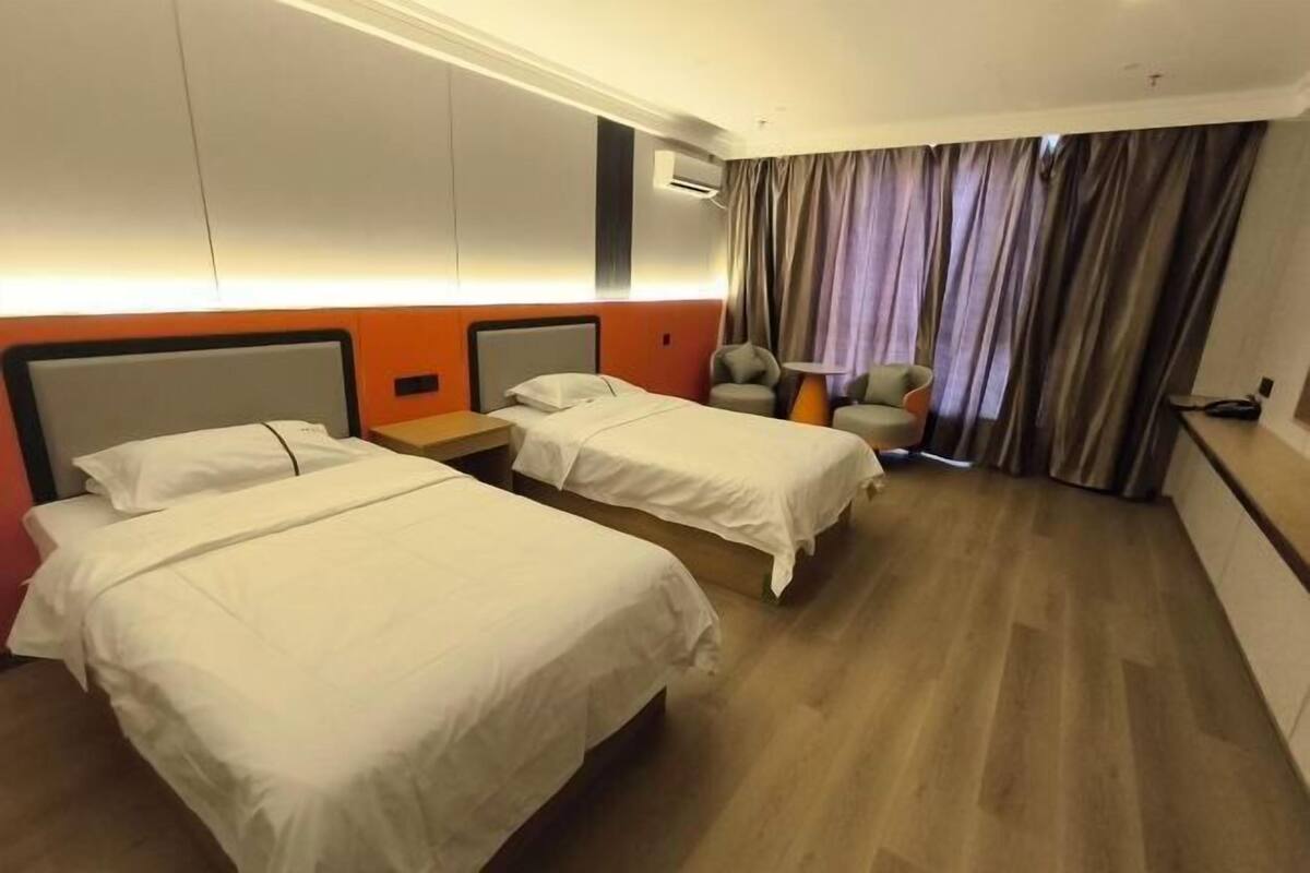 A hotel room with two beds, a nightstand, a chair, and a large window with curtains.