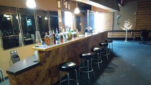 Uma área de bar com balcão de madeira, vários bancos e um espelho.