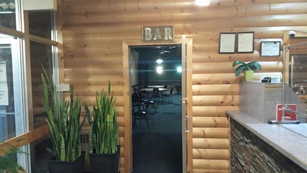 Interior de madeira com um letreiro 'BAR', plantas em vasos e um balcão com um quadro de cardápio.