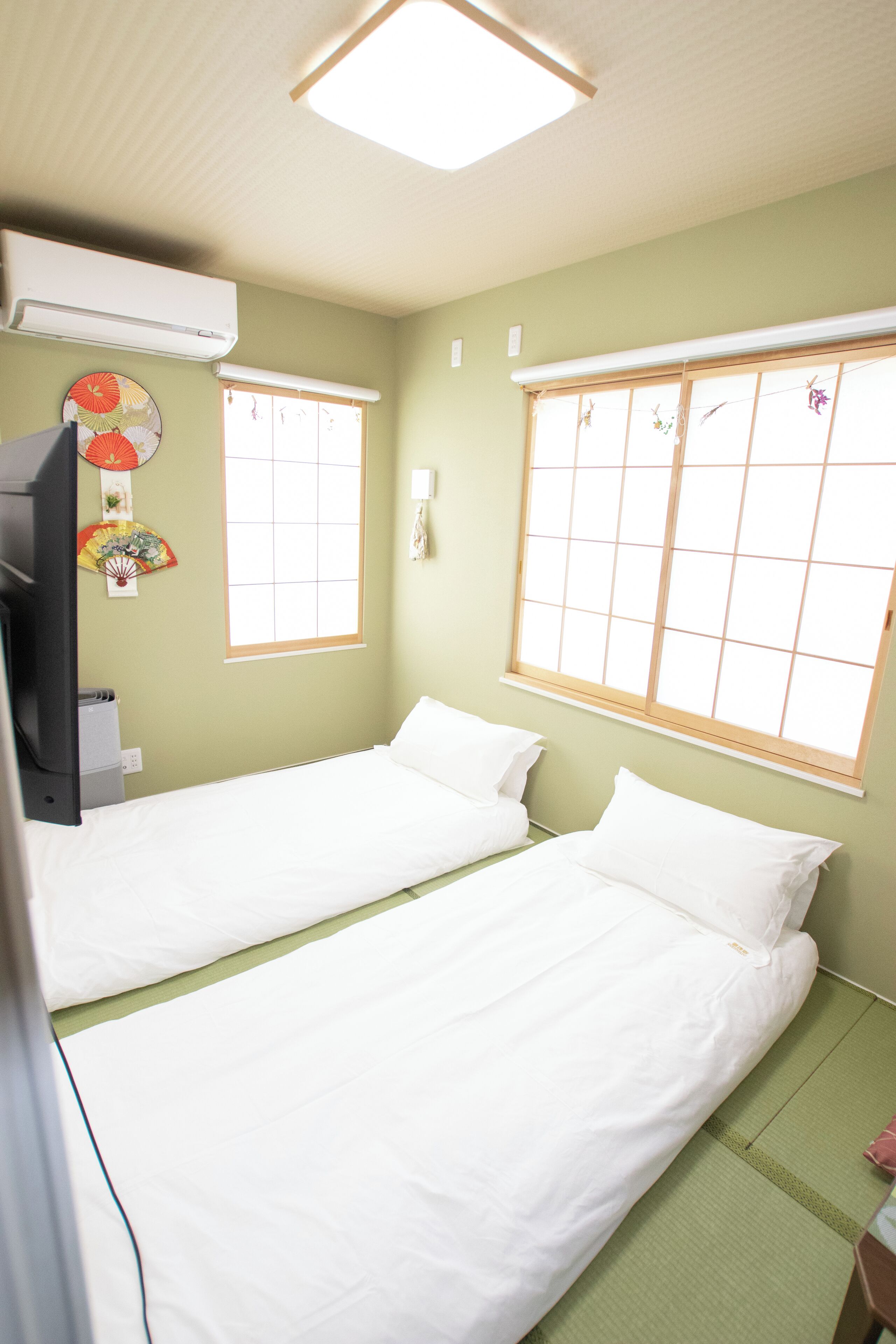 A room with two single beds, a television, and a window with a view of the outside.