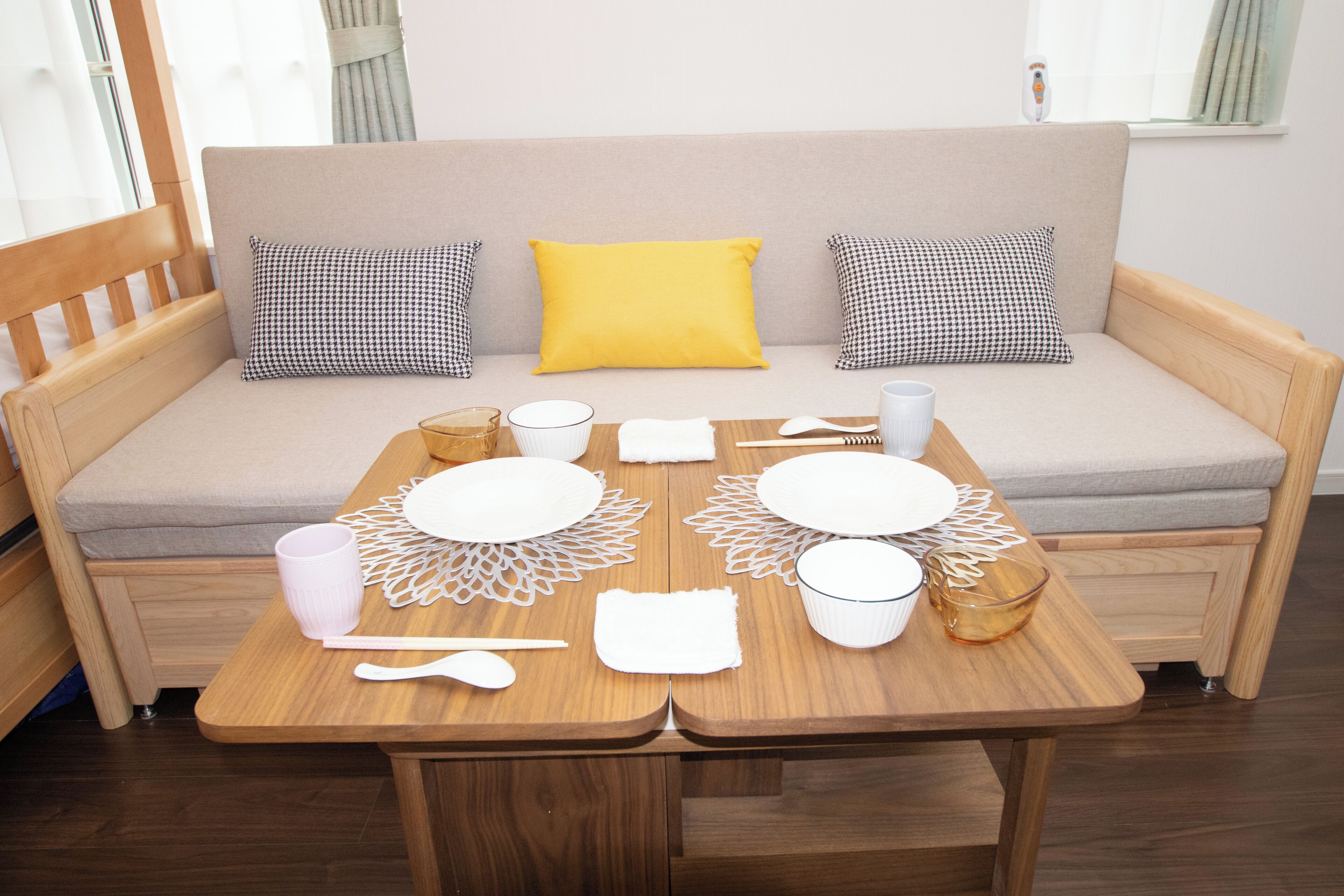 A cozy living area with a sofa, a wooden table set for dining, and a window with curtains.